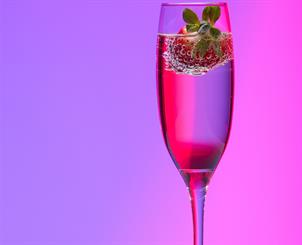 Das Bild zeigt ein Sektglas mit Erdbeere auf einem rosaroten u violetten Hintergrund.