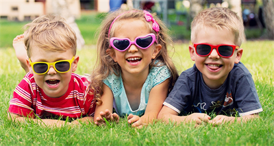 Das Bild zeigt drei Kinder mit Sonnenbrille, die im Gras liegen.