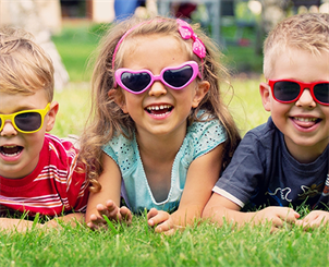 Das Bild zeigt drei Kinder mit Sonnenbrille, die im Gras liegen.